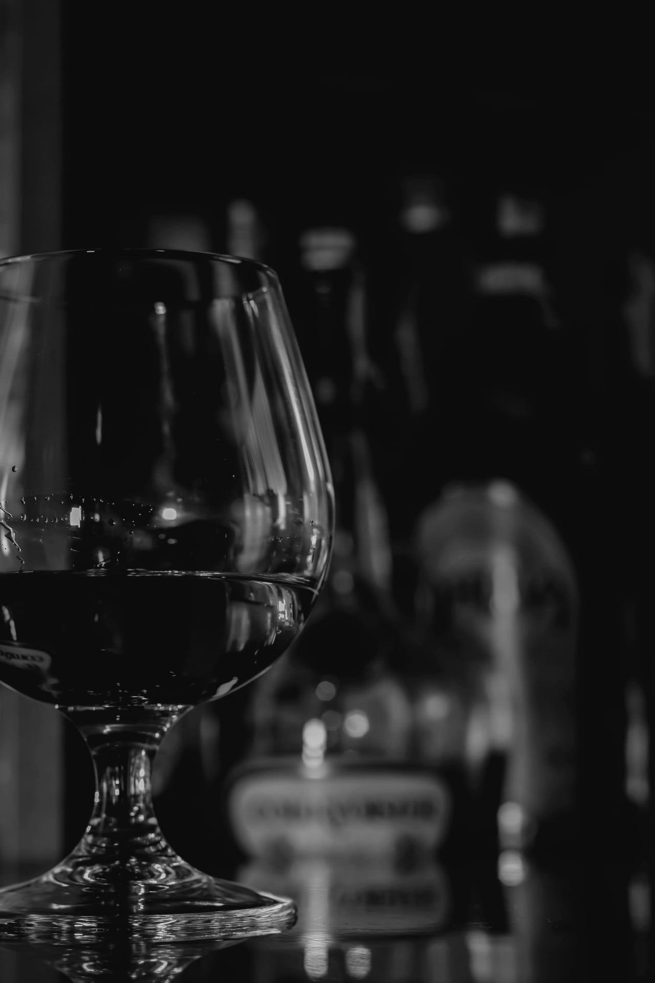 Verre de cognac sur un bar en bois, lumière chaude tamisée.